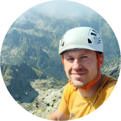 Osoba w kasku wspinaczkowym na tle górskiego krajobrazu.
