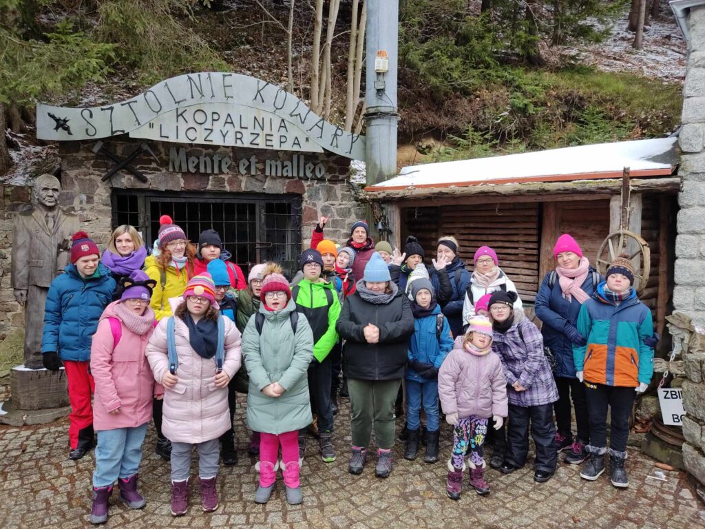 Grupa dzieci i dorosłych w kolorowych kurtkach przed wejściem do kopalni Liczyrzepa w Kowarach.