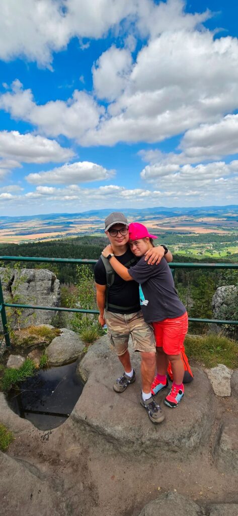 Dwoje ludzi przytula się na szczycie góry z pięknym widokiem na dolinę i niebo pełne chmur.