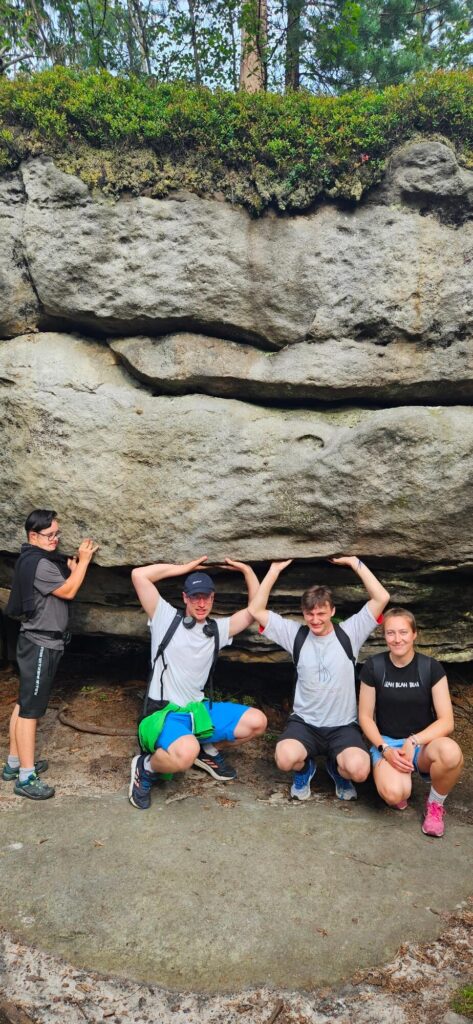 Czworo osób pozuje, udając, że podtrzymują wielki, płaski głaz w lesie.