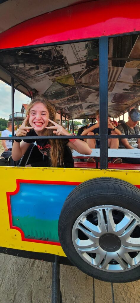 Dziewczyna uśmiecha się i pokazuje gest V w kolorowym wagonie z obrazkami na suficie.