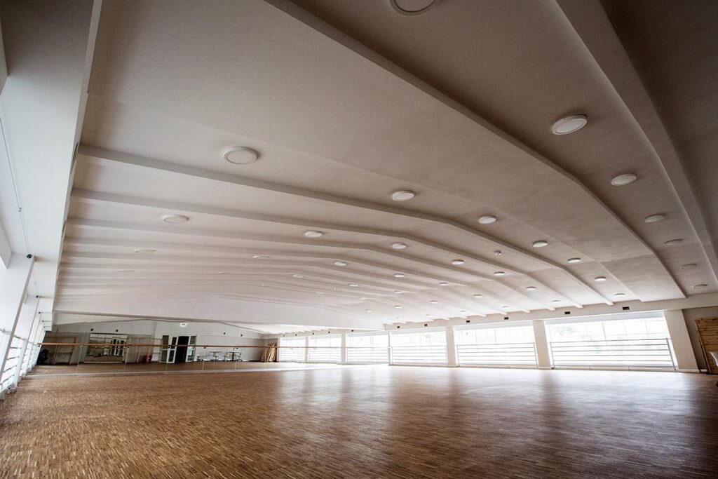 Duża, jasna sala z drewnianą podłogą i lustrami, idealna do zajęć tanecznych lub treningowych.