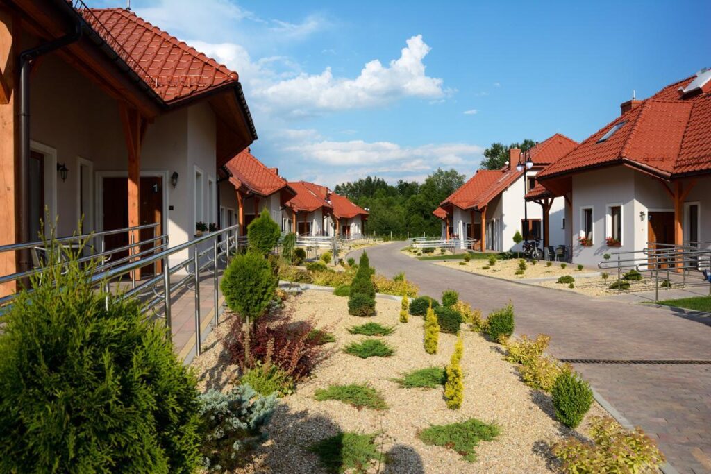 Nowoczesne domy z czerwonymi dachami przy alejce, otoczone starannie zaprojektowanym ogrodem, pod błękitnym niebem.