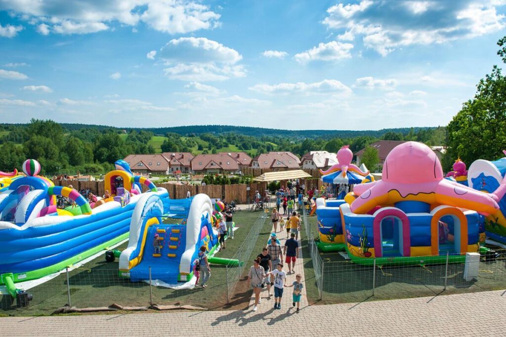 Park z dmuchawcami, kolorowe zjeżdżalnie i place zabaw, ludzie cieszą się słonecznym dniem na wsi.