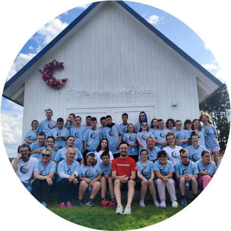 Grupa ludzi w niebieskich koszulkach pozuje do zdjęcia przed białym budynkiem z napisem to the moon and back.