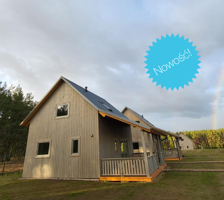 Drewniane domki w otoczeniu natury. Na zdjęciu z naklejką Nowość! i widoczną tęczą w tle.